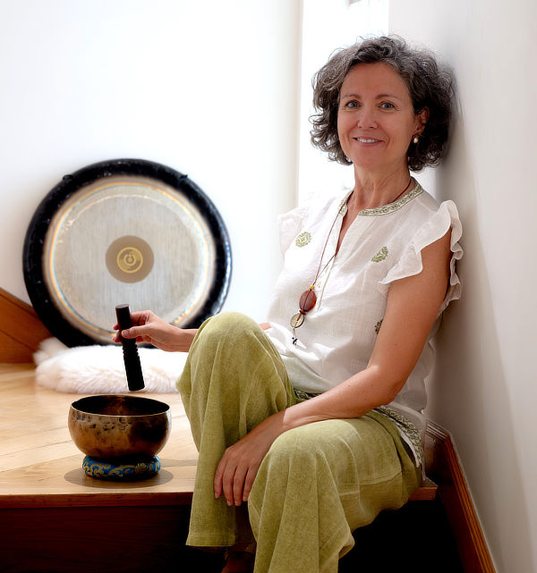 Olga Muñoz sentada junto a un gong y un cuenco tibetano, sonriendo
