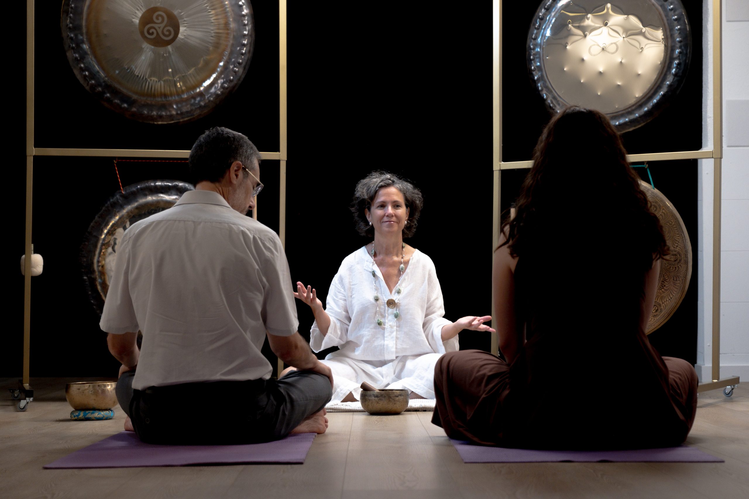 Olga Muñoz guiando una sesión de gong con dos personas sentadas frente a gongs y cuencos