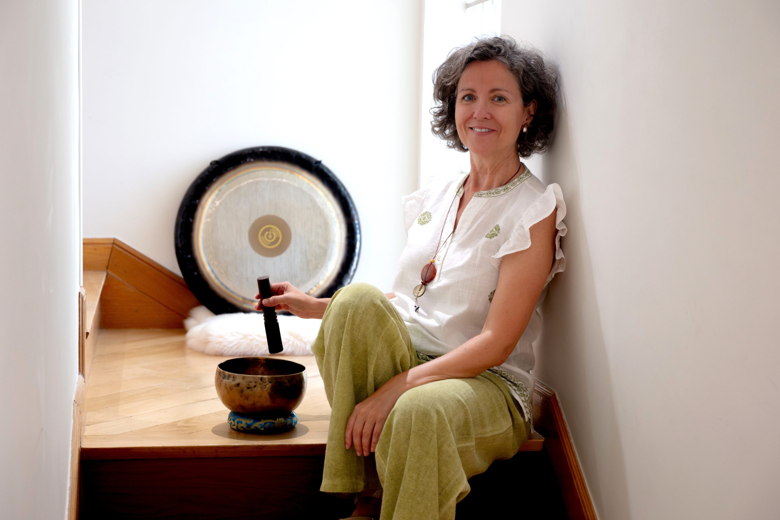 Olga Muñoz sentada junto a un gong y un cuenco tibetano, sonriendo